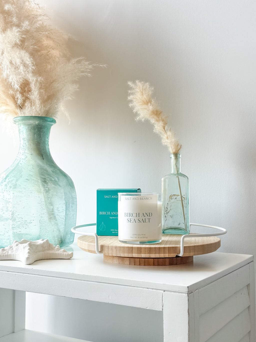 Candle and packaging on a wooden tray with decorative vases and pampas grass Birch and Sea Salt -Salt and Branch
