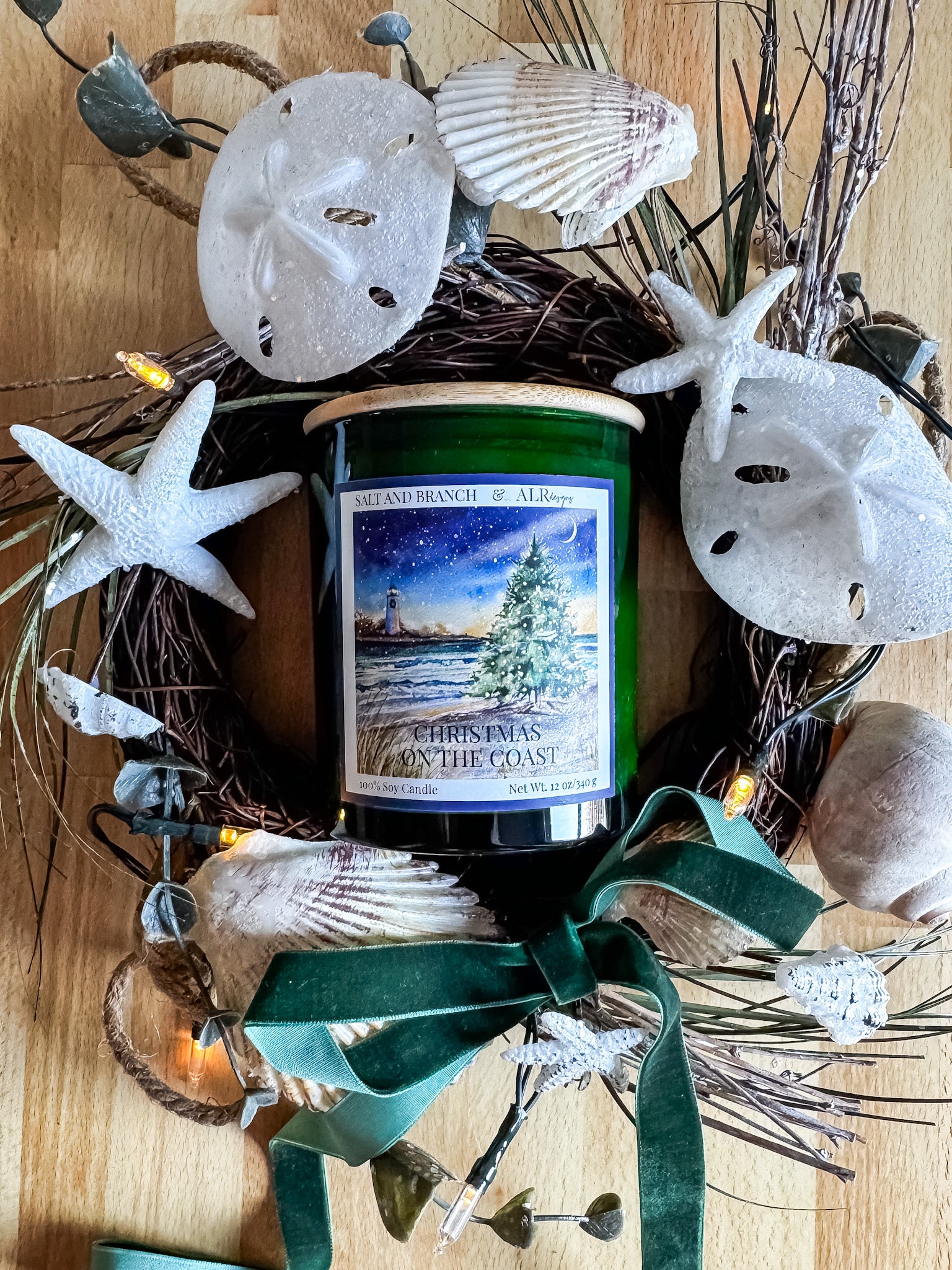 Candle with a Christmas-themed label surrounded by a seashell wreath on a wooden surface