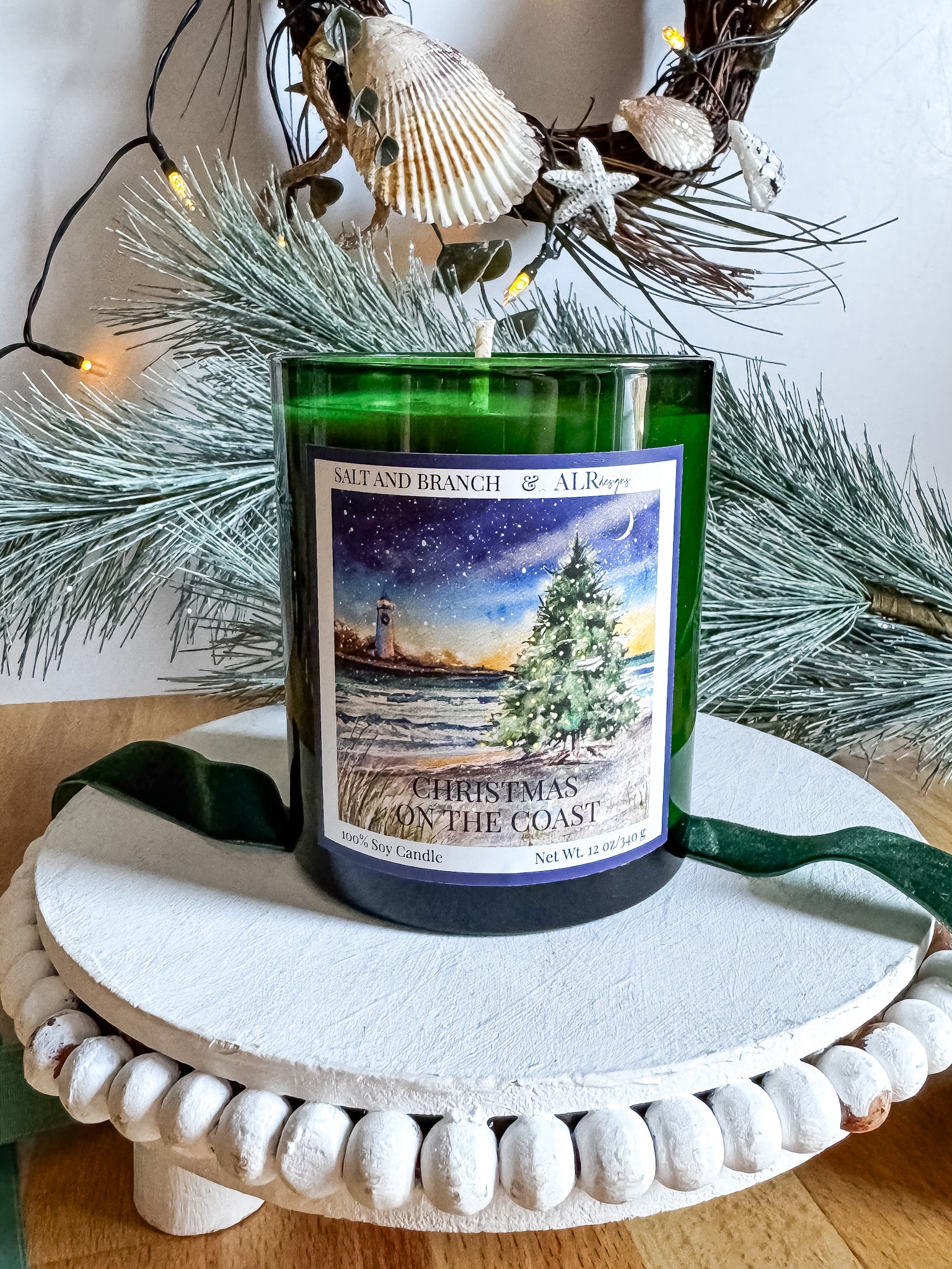 Candle in a green vessel with a Christmas on the Coast label on a decorative stand.