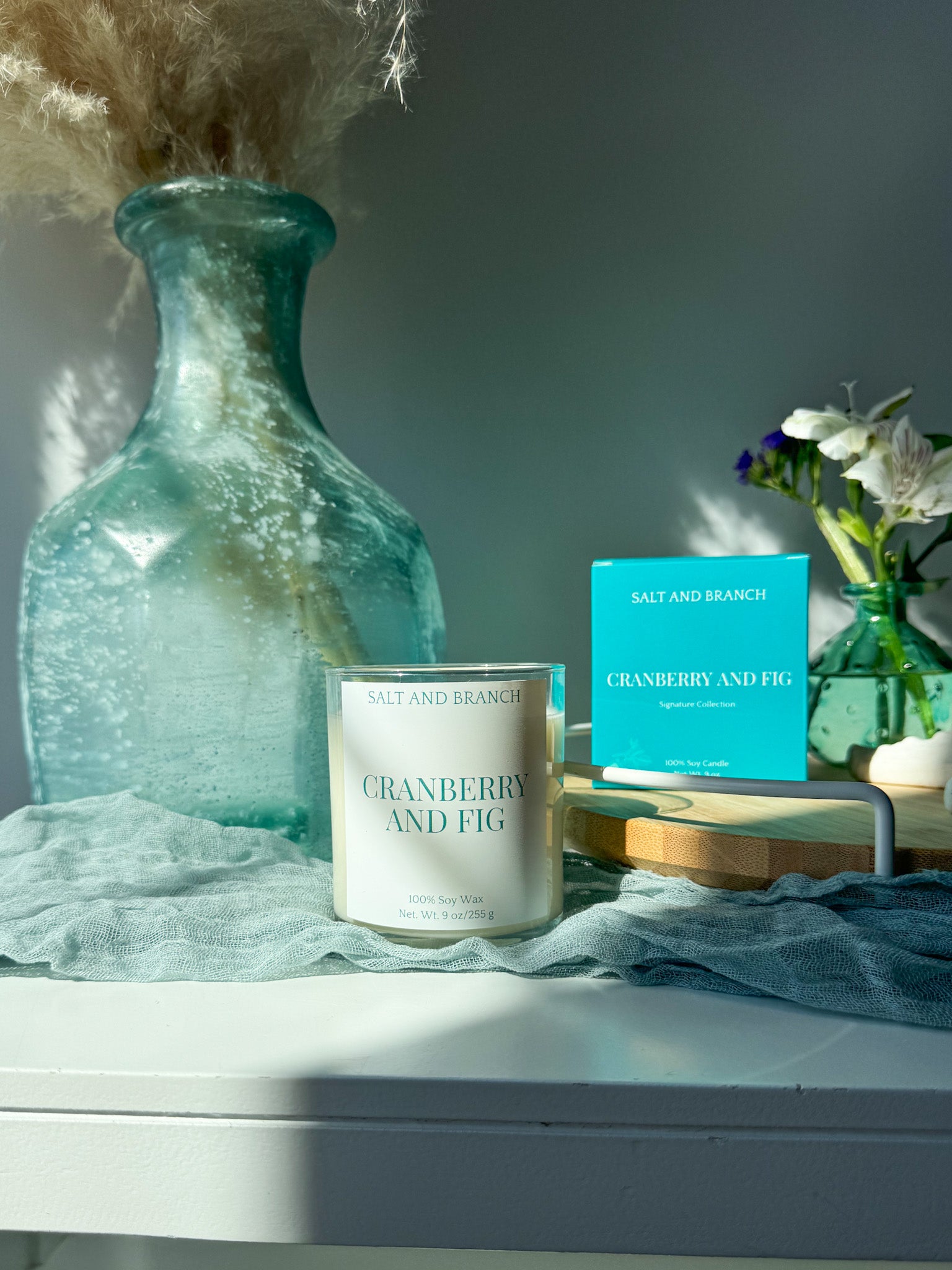 Candle and packaging with 'Cranberry and Fig' scent on a surface with decorative elements. Salt and Branch
