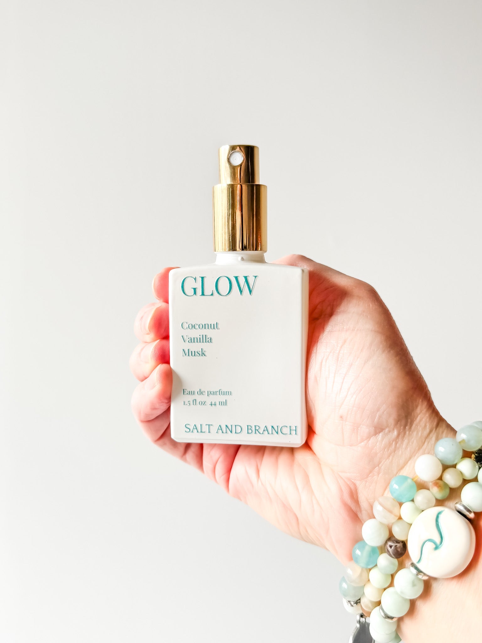 Hand holding a 'GLOW' perfume bottle with a plain background