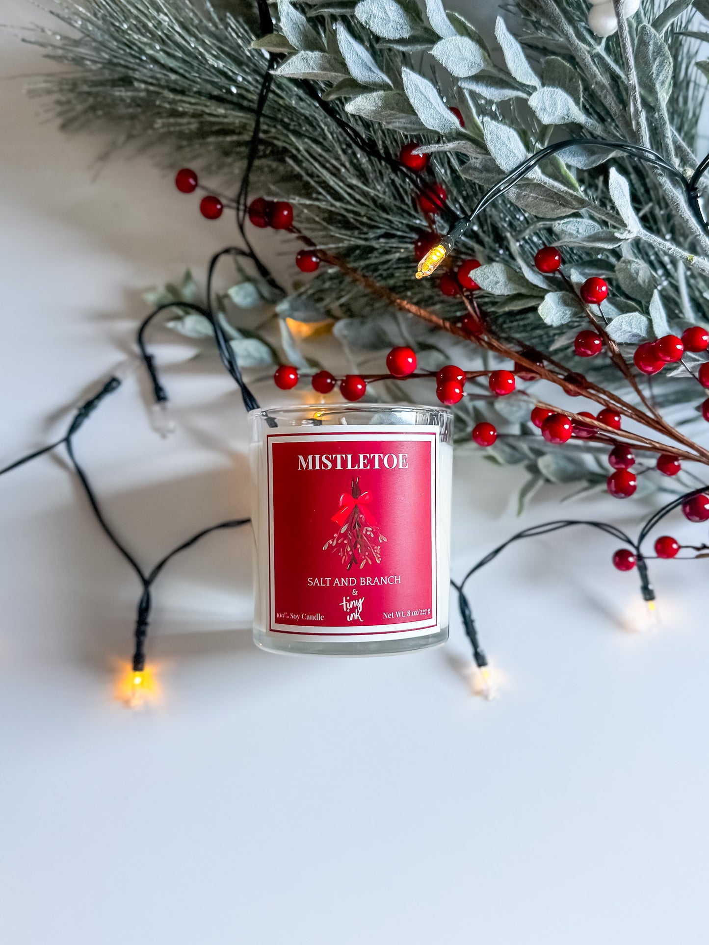 Candle labeled 'Mistletoe' with Christmas decorations on a white background