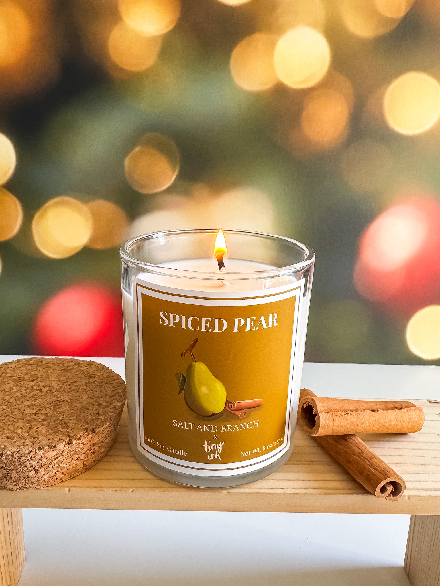 Spiced pear candle with cinnamon sticks on a wooden surface with Christmas lights in the background