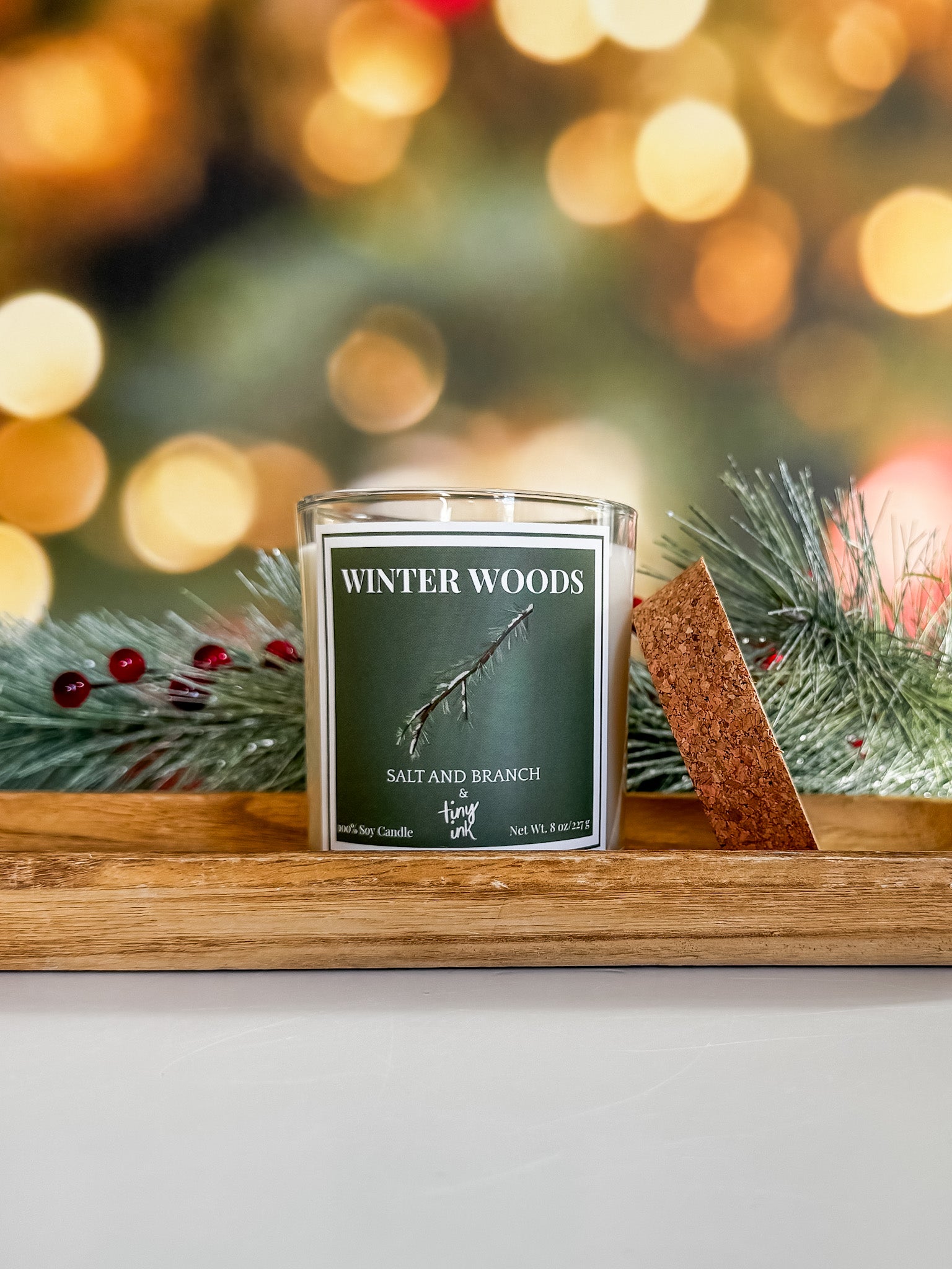 Candle labeled 'Winter Woods' on a wooden tray with festive background