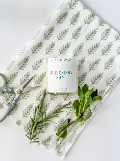 Rosemary Mint Soy Candle on teal towel with fresh herbs Salt and Branch