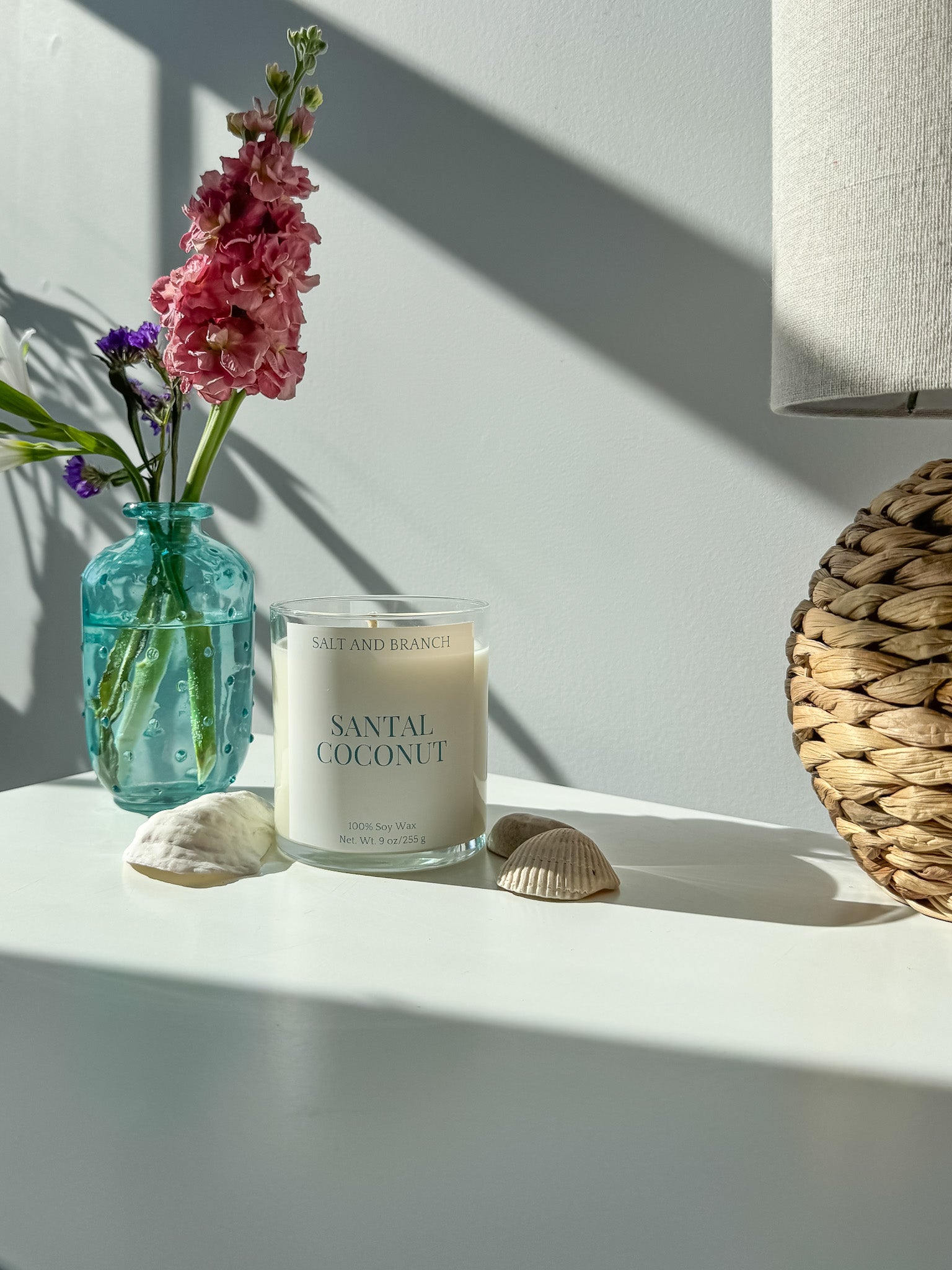 Santal Coconut soy candle with a vase of flowers and seashells on a light surface - Salt and Branch